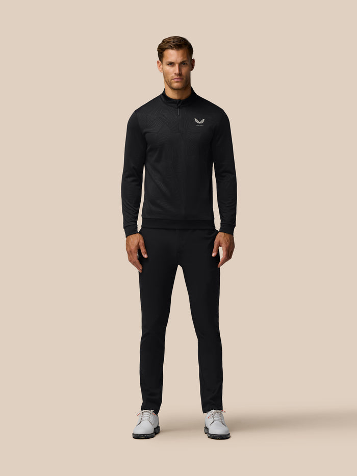 Man wearing black Golf Club Classic 1/4 Zip Debossed Top with subtle all over print against a beige backdrop