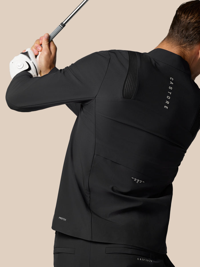 Side view of golfer wearing a black Castore Golf Pinnacle LVS jacket holding a golf club with a white glove
