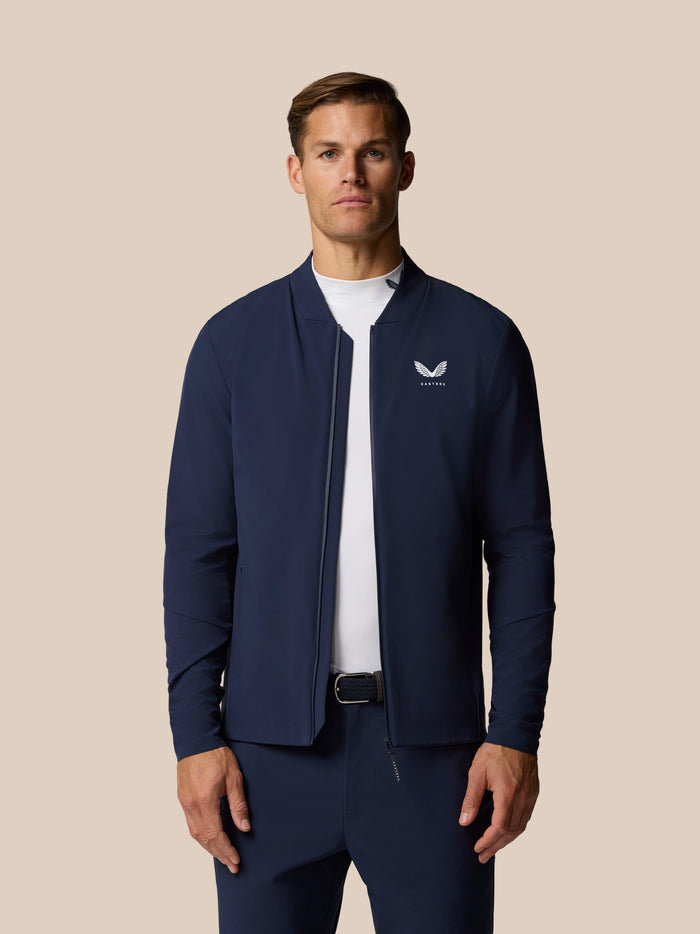 Three quarter back view of male model in navy Castore LVS jacket showing vertical logo on the upper back