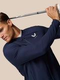 Male model wearing Midnight Navy Golf Pinnacle LVS Winter Jacket swinging a golf club in a studio against a beige background.