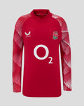 Junior England pre match drill top in red with a white rose crest on the chest and Castore logo, sleeves feature a white geometric pattern