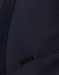 Water droplets bead on navy CORE HOLDALL fabric showing water resistance and PROTEK badge