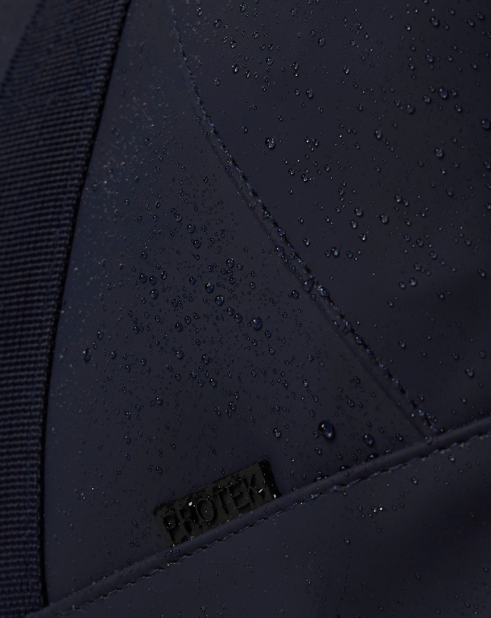 Water droplets bead on navy CORE HOLDALL fabric showing water resistance and PROTEK badge