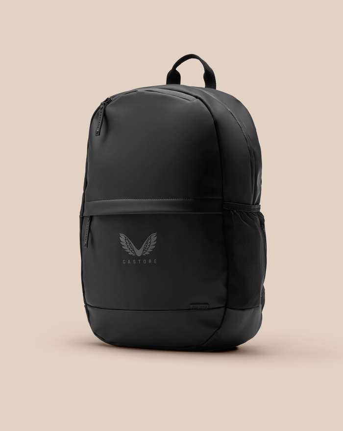 Core Backpack in matte black with top handle, front zip pocket, side mesh pocket, PROTEK tag, and Castore wing logo