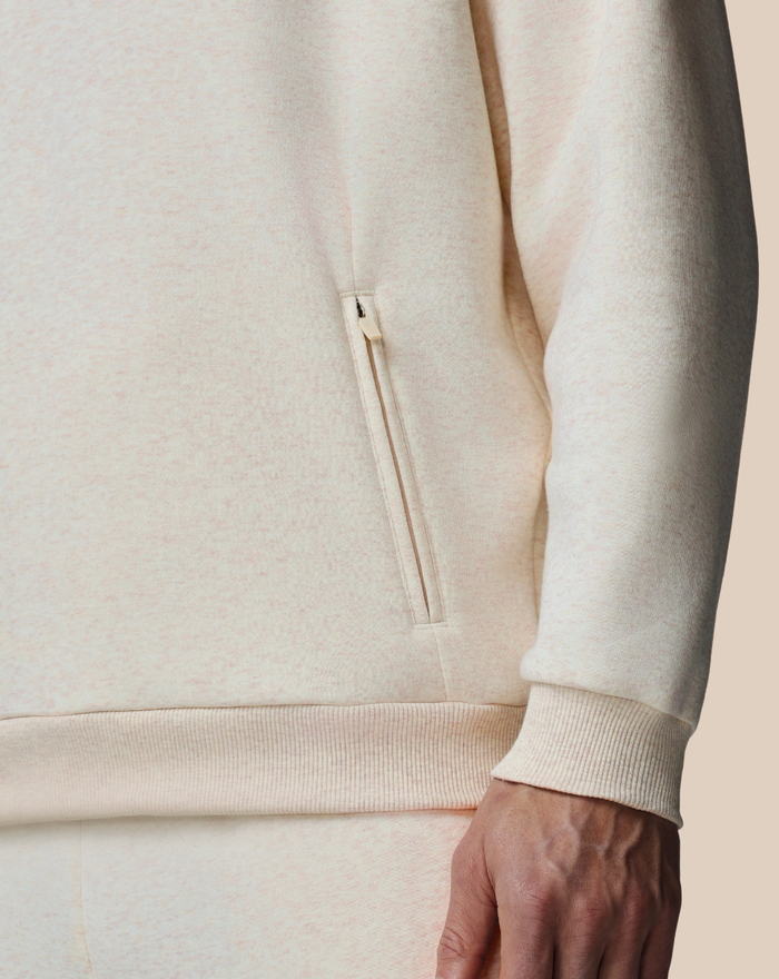 Beige cotton fleece hoodie close up highlighting a zippered side pocket and ribbed hem